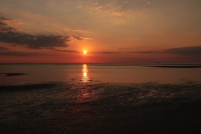 the sun is setting over the water on the beach